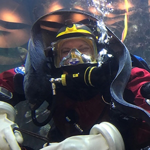 A diver smiling while a wolf eel swims above their head.