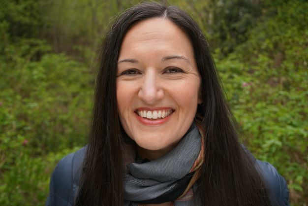 Dr. Erin Meyer smiling in front of a leafy backdrop.