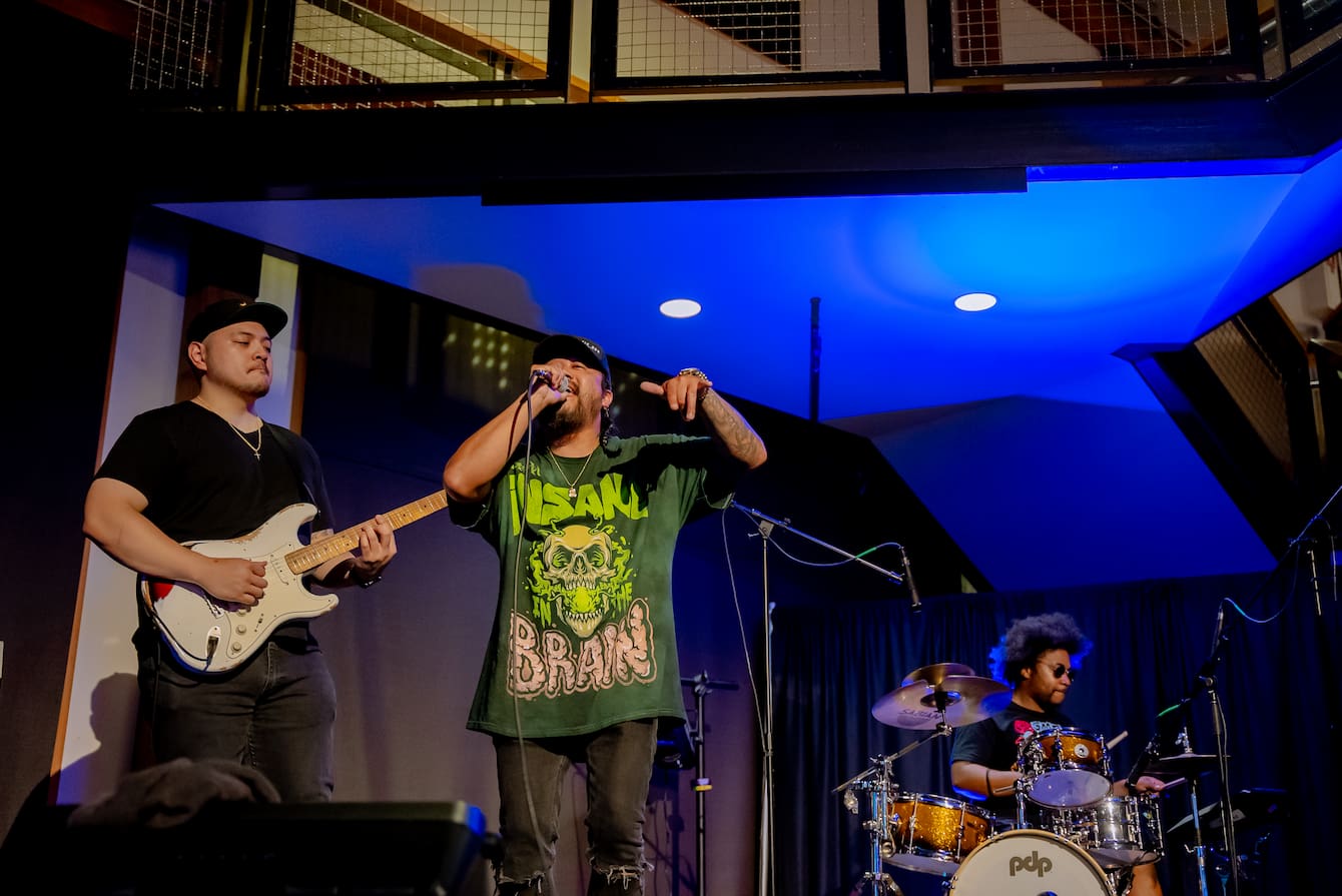 A guitarist, vocalist and drummer giving a performance onstage in Puget Sound Hall.